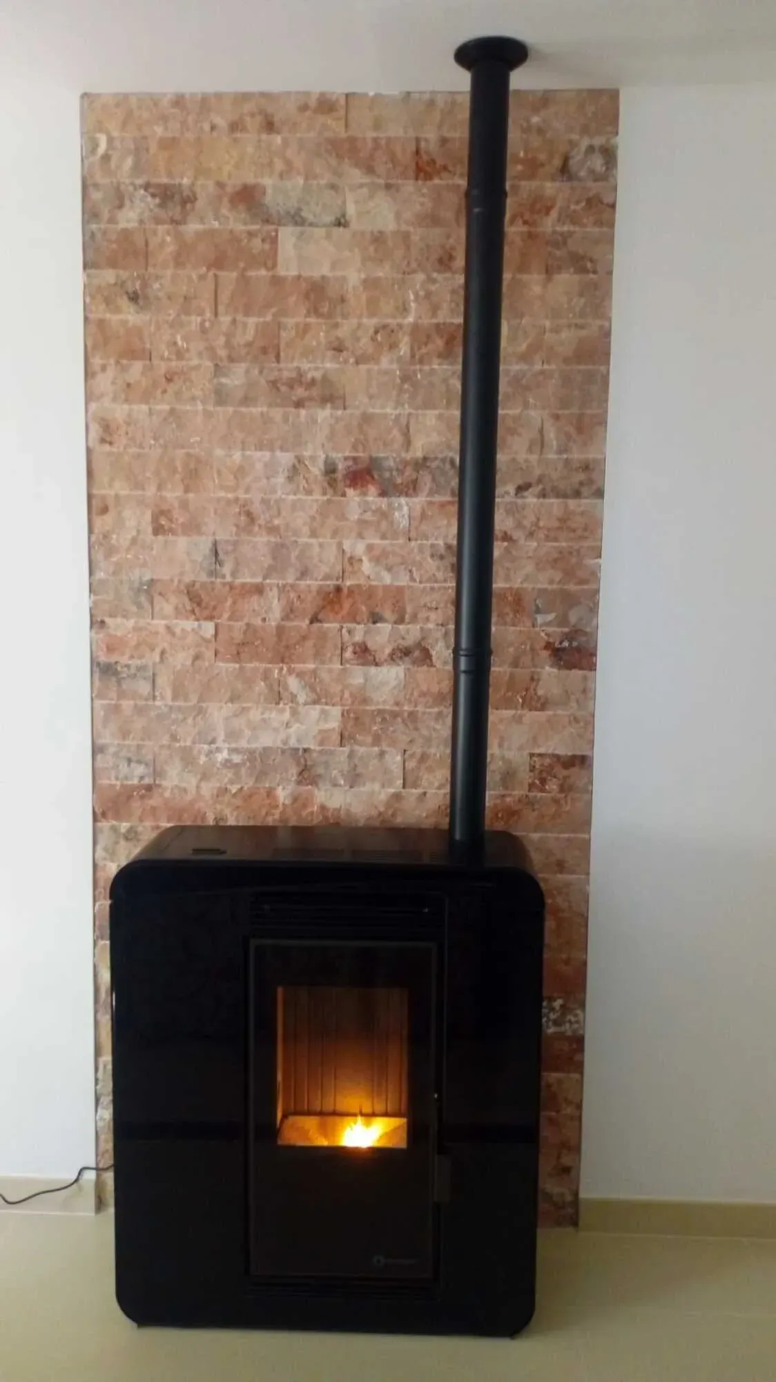 Estufa de leña negra con fuego encendido y una alta chimenea negra adosada a una pared de ladrillos.