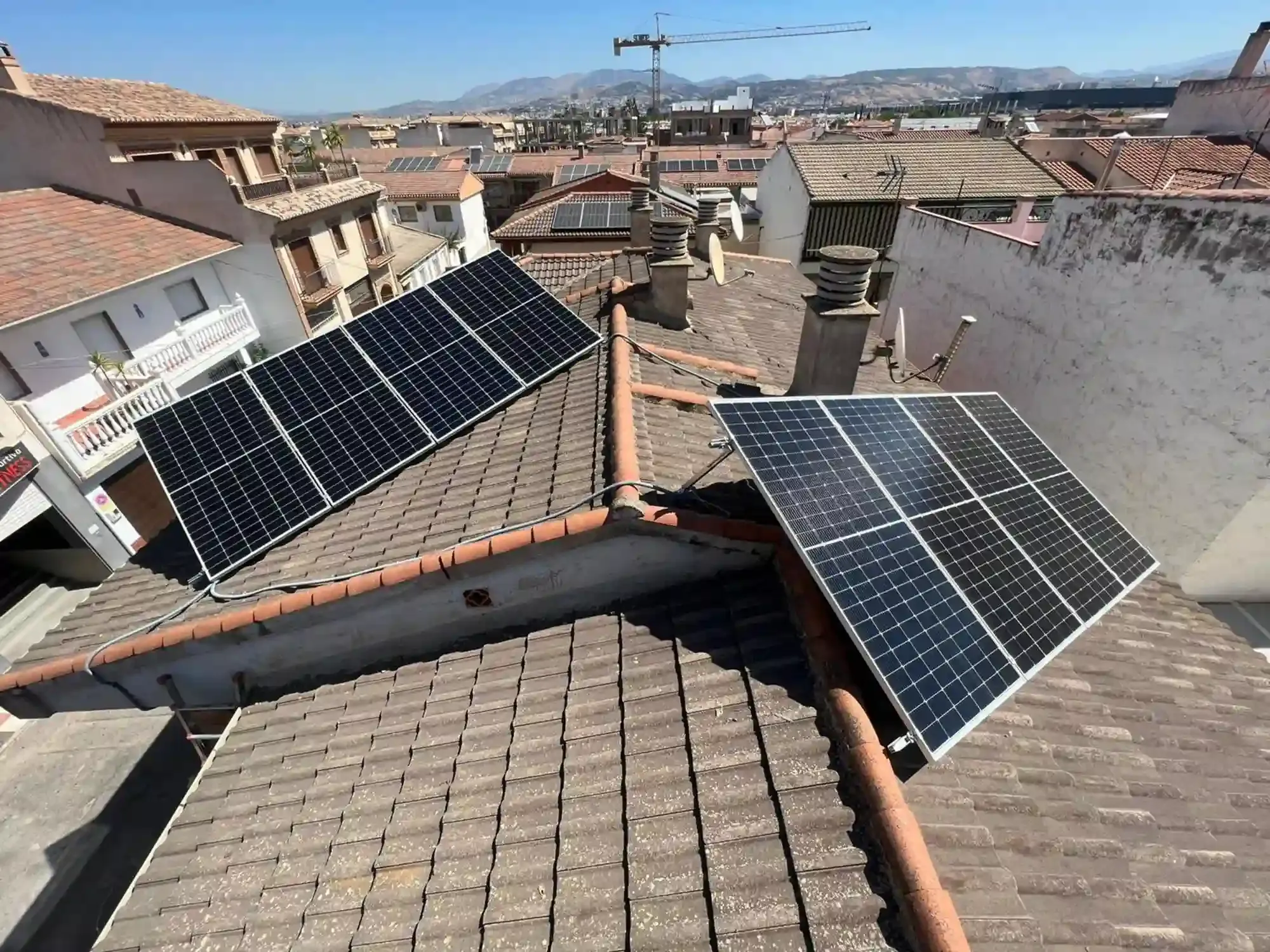 Paneles solares en los tejados de edificios con tejas en una ciudad densamente poblada bajo un cielo despejado.