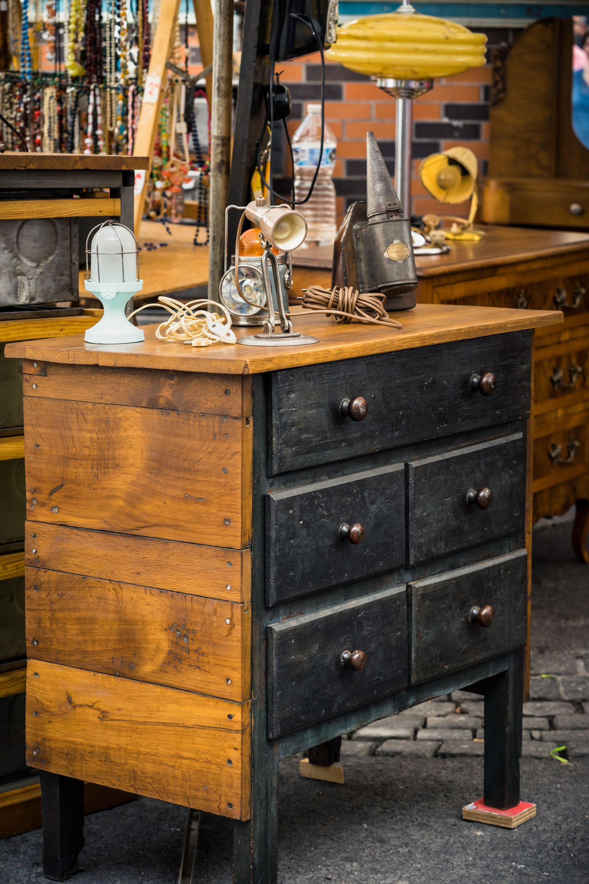Commode rustique en bois avec tiroirs noirs exposée sur un étal de marché en plein air