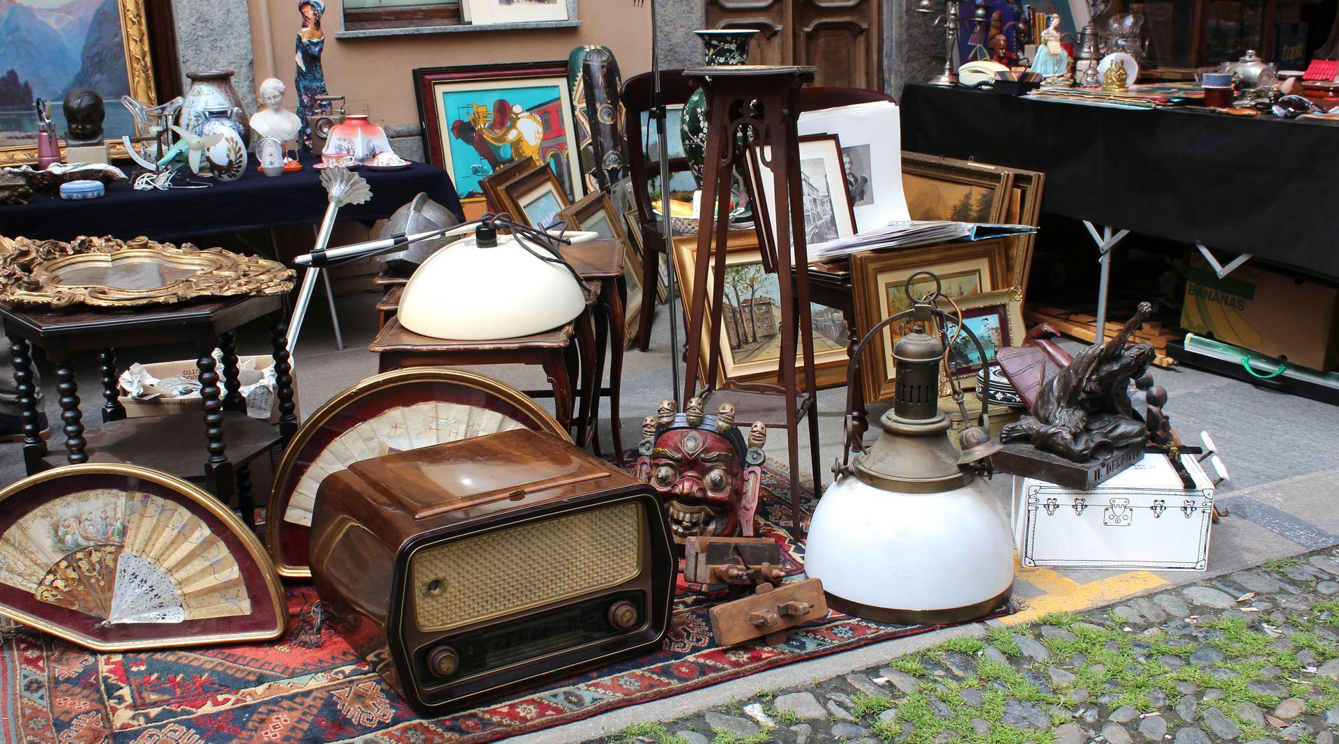 Des radios anciennes, des ventilateurs et des tableaux encadrés exposés dans un marché aux puces en plein air.