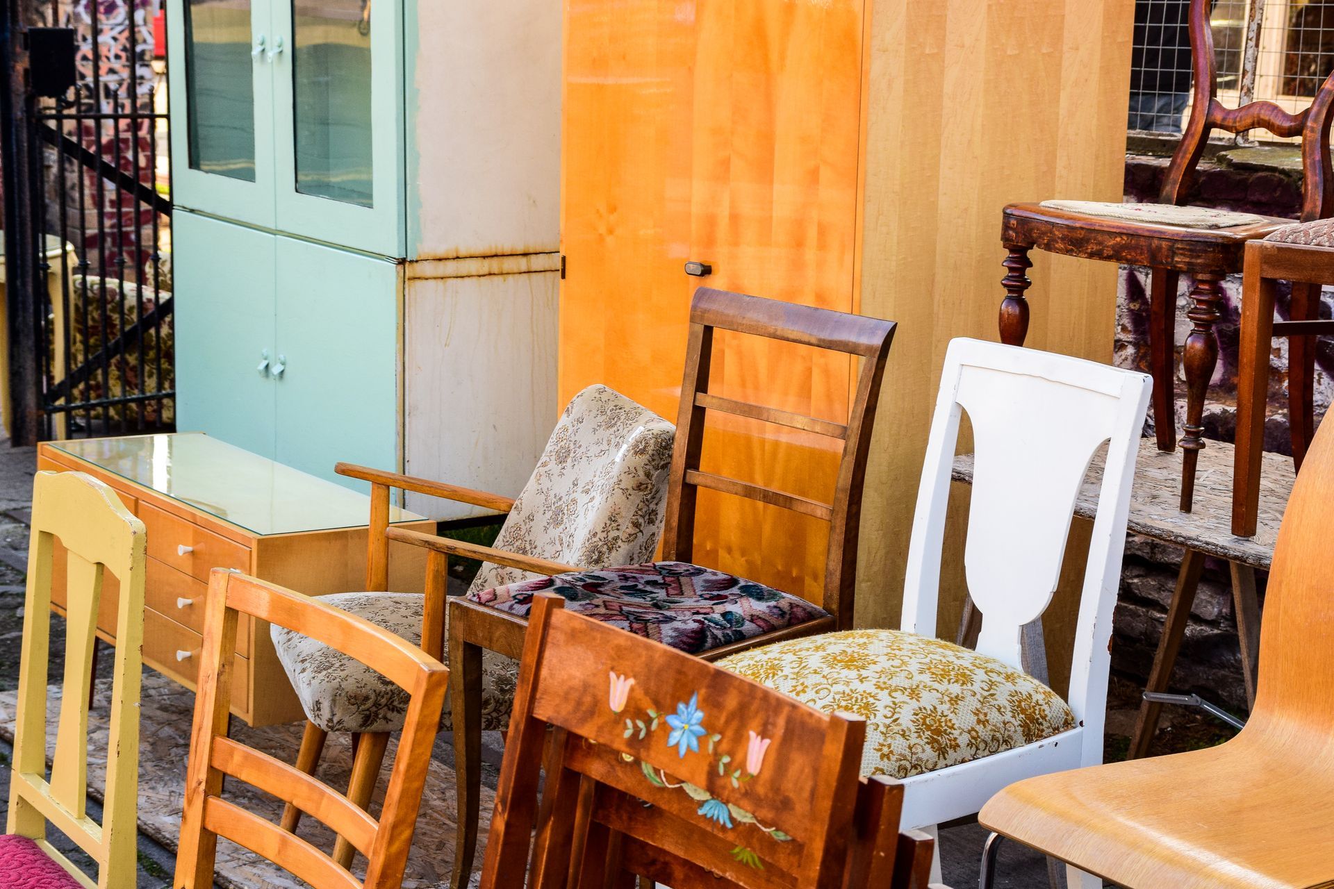 Des chaises et des tabourets de différentes sortes sont disposés à l'extérieur, à côté d'une armoire bleu clair et d'un mur orange.