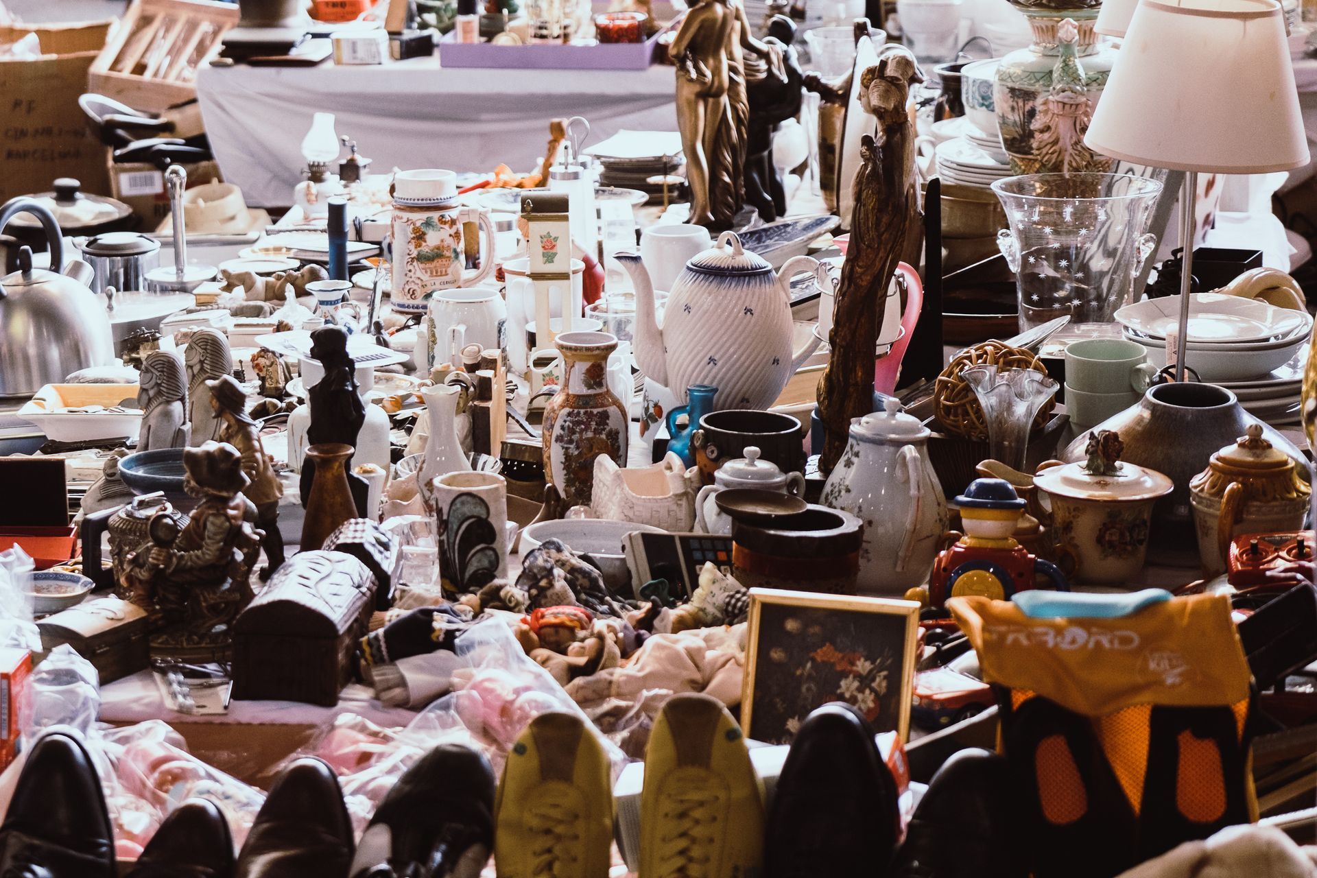 Table de marché aux puces bondée, remplie de céramiques, de lampes et d'objets ménagers vintage assortis.