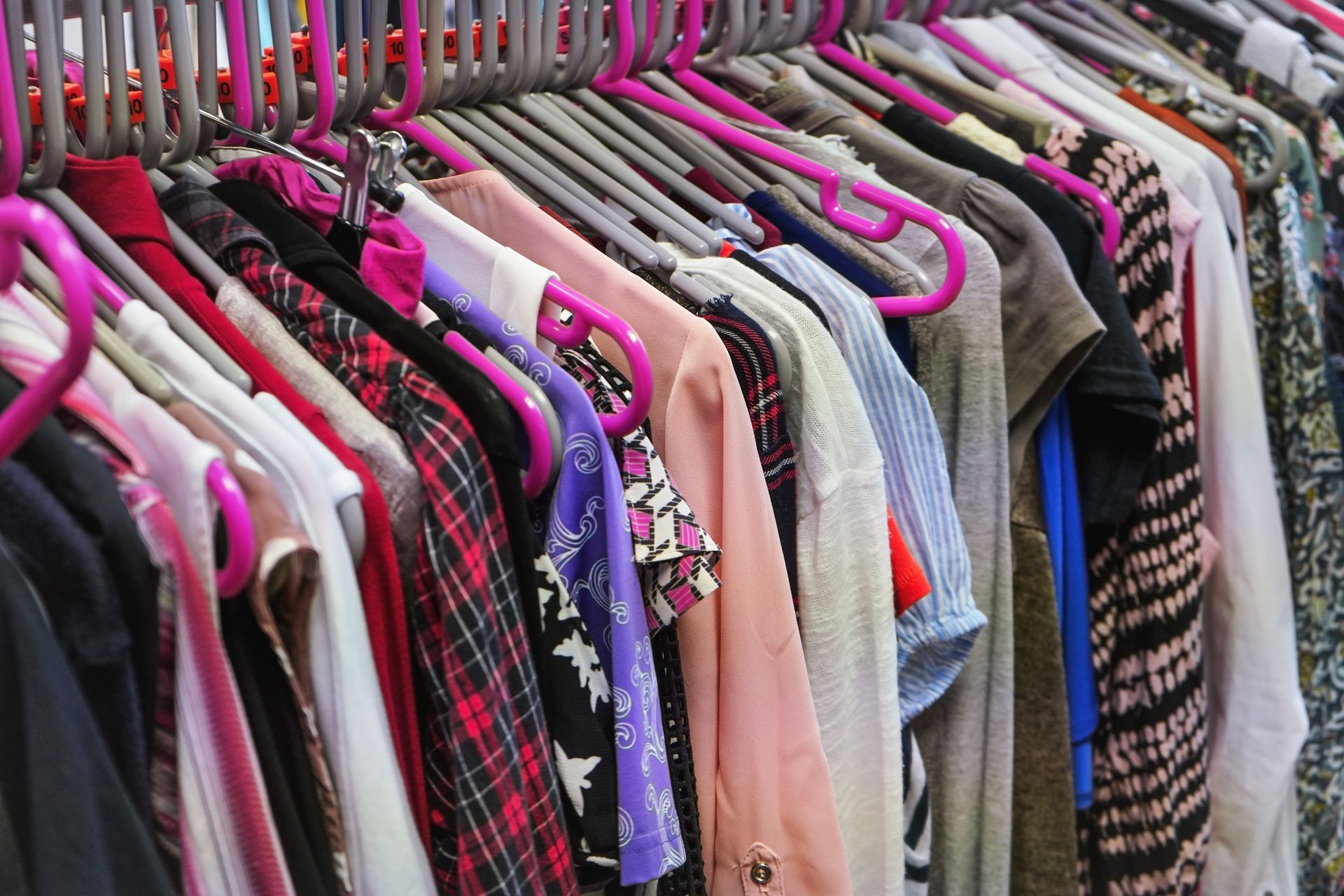 Des vêtements suspendus à un portant, présentant un assortiment de chemises et de vestes roses, noires, grises et beiges.