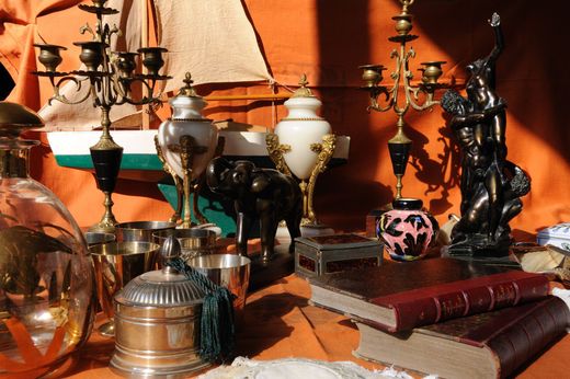 Lampes anciennes, verrerie et livres divers disposés sur une table devant un mur orange.