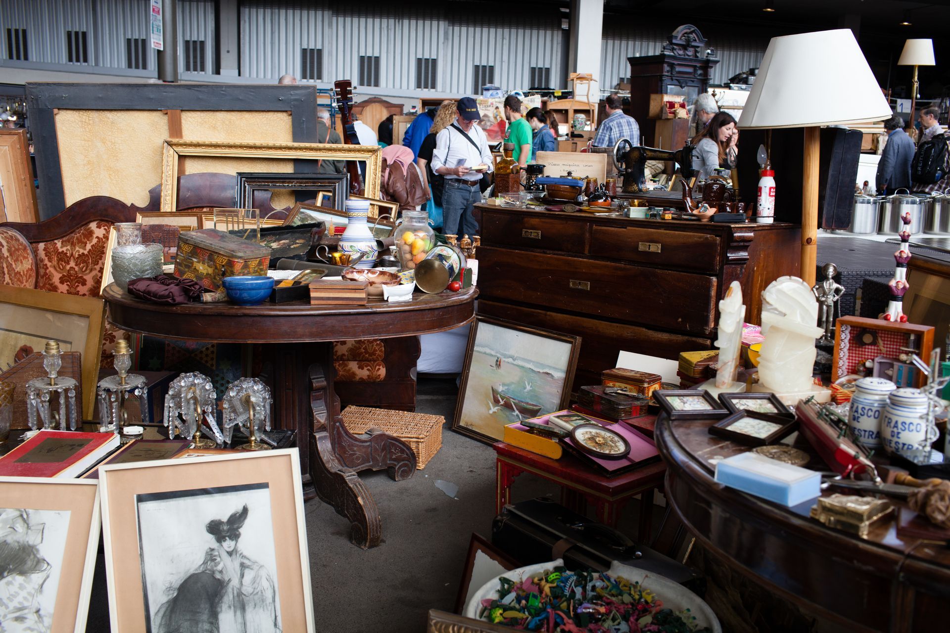 Un étal de marché aux puces intérieur regorgeant d'antiquités, de tableaux encadrés, de poteries et d'objets vintage divers.