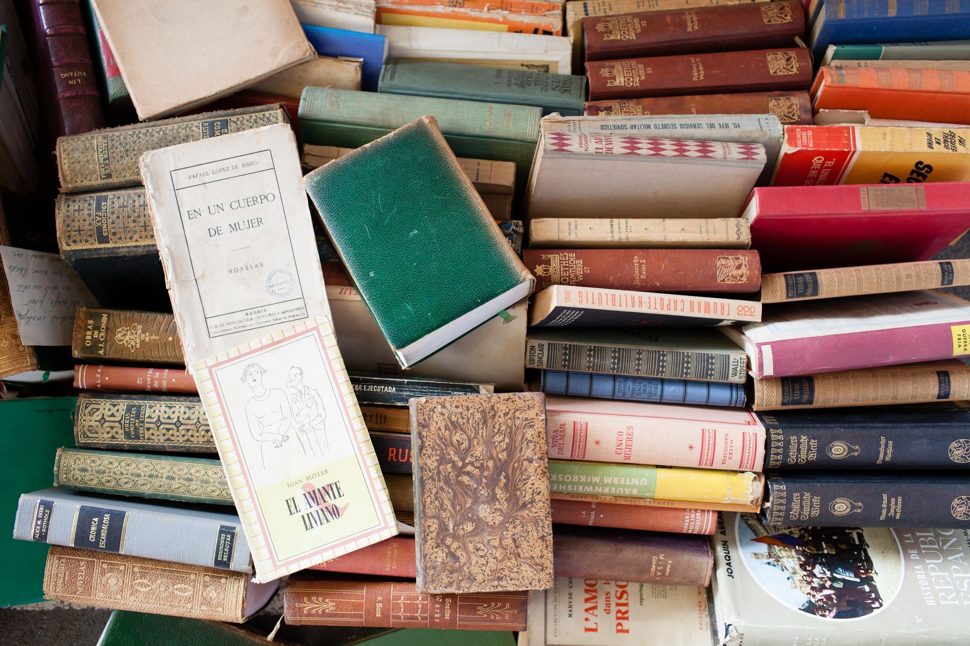 Pile de livres anciens divers, pêle-mêle, aux dos usés et aux couvertures colorées.