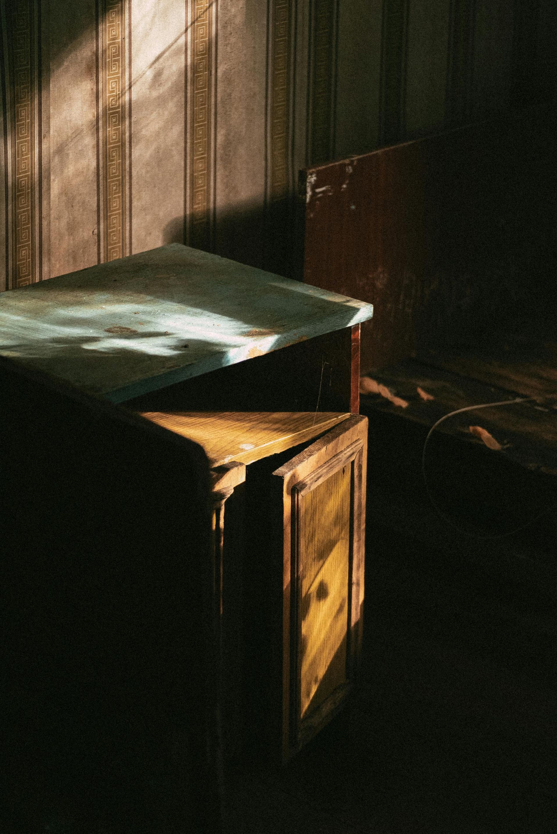 Armoire en bois baignée de soleil dans une pièce sombre, la lumière se diffusant sur sa surface et sur le mur derrière elle.