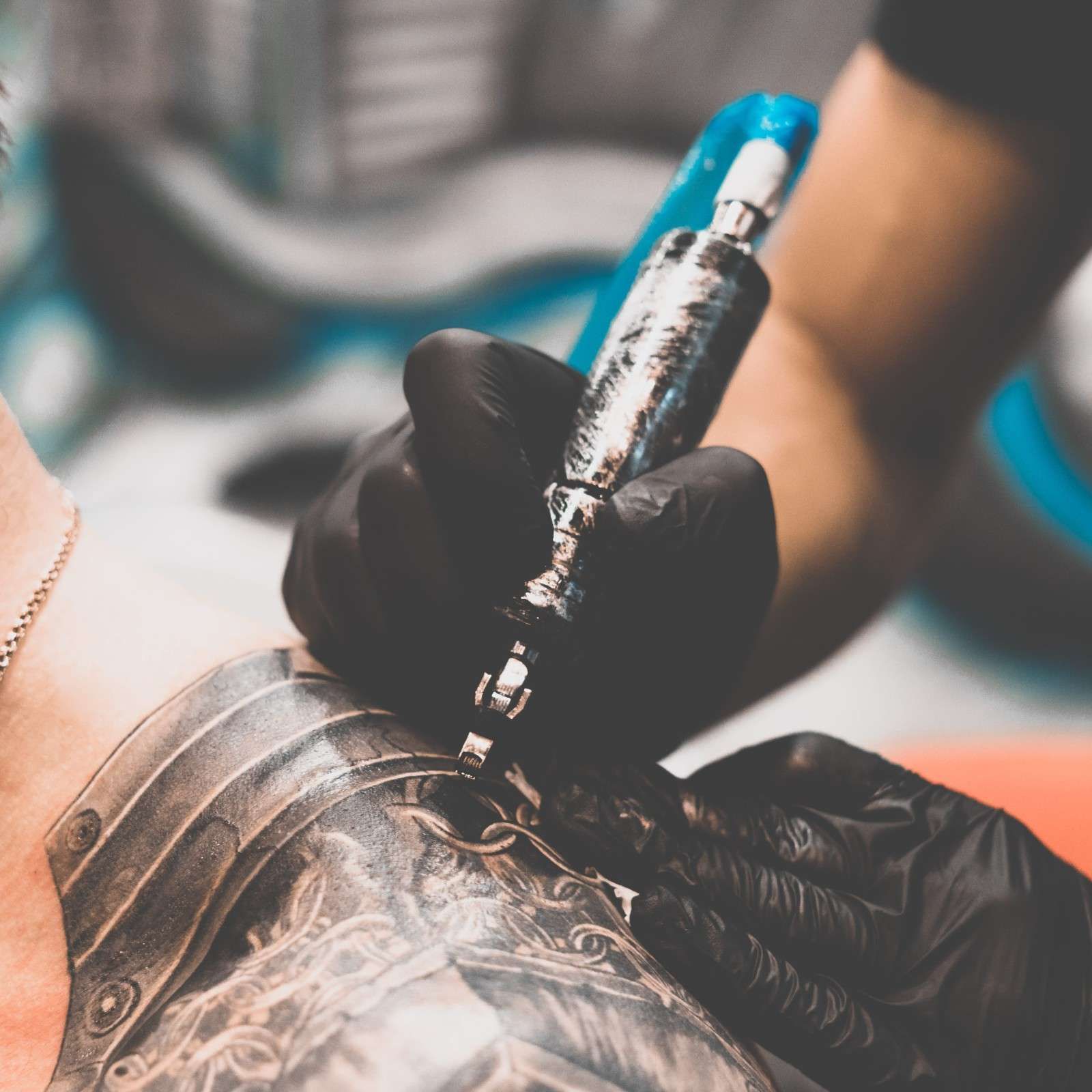 Un artista del tatuaje que usa guantes negros utiliza una máquina de tatuar tipo bolígrafo para tatuar un diseño 