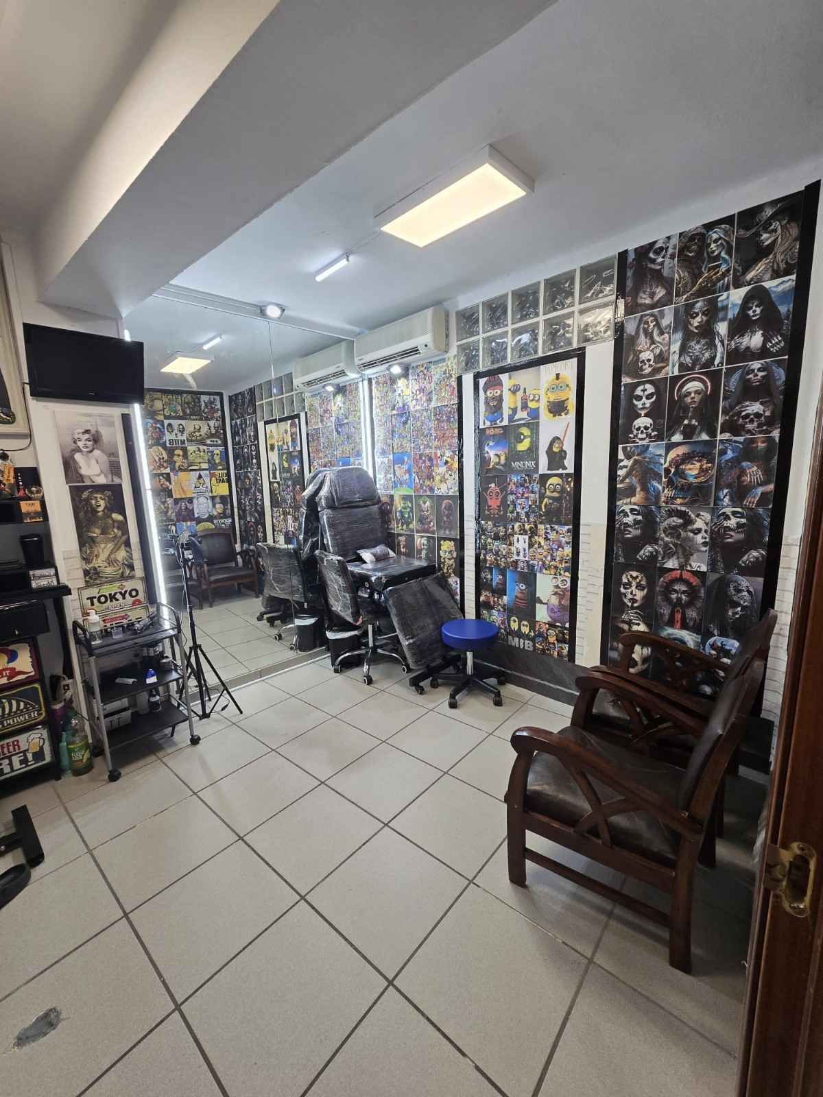 Un salón de tatuajes con una silla de tatuaje profesional, un taburete con ruedas, mesas para equipos 