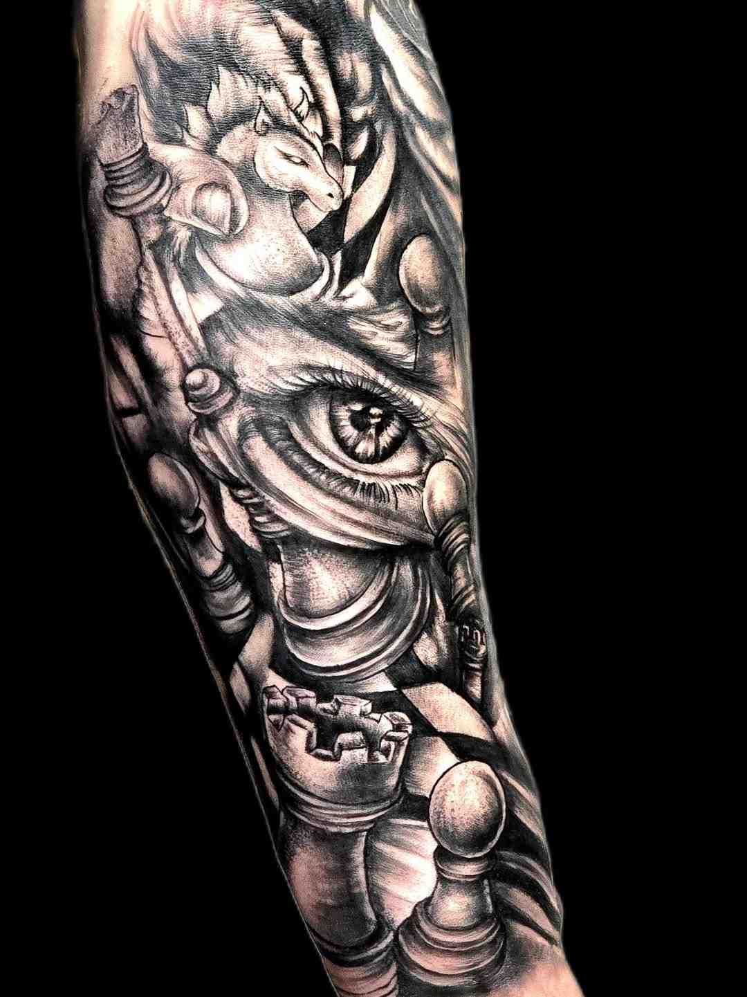 Tatuaje negro y gris en un brazo que presenta un ojo humano realista integrado con varias piezas de ajedrez.