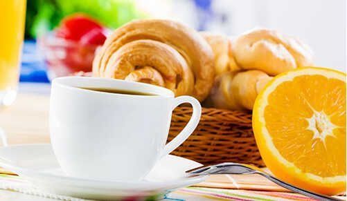 Taza de café blanco con pasteles y rodajas de naranja sobre una mesa