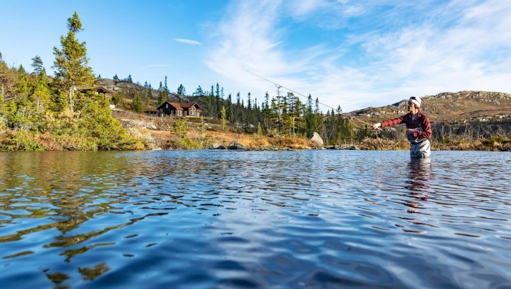 Ein Mann angelt in einem See mit Bergen im Hintergrund.