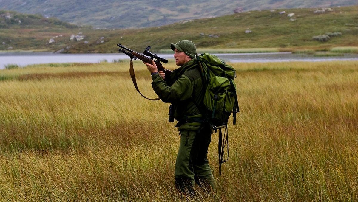Ein Jäger auf einem Feld mit einem Rucksack, Gewehr und Ausrüstung
