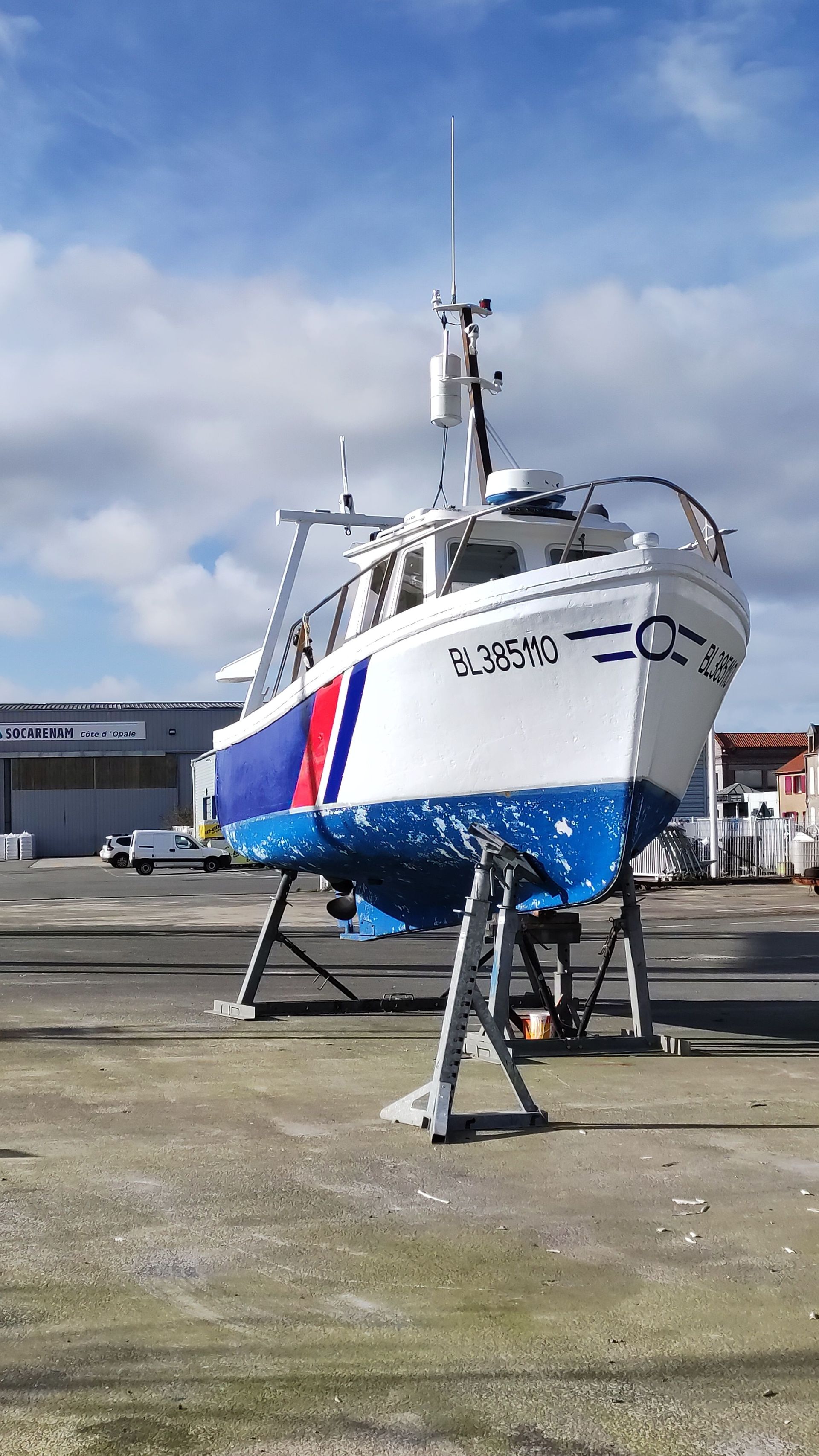 Bateau sur supports métalliques dans un chantier naval sous un ciel nuageux