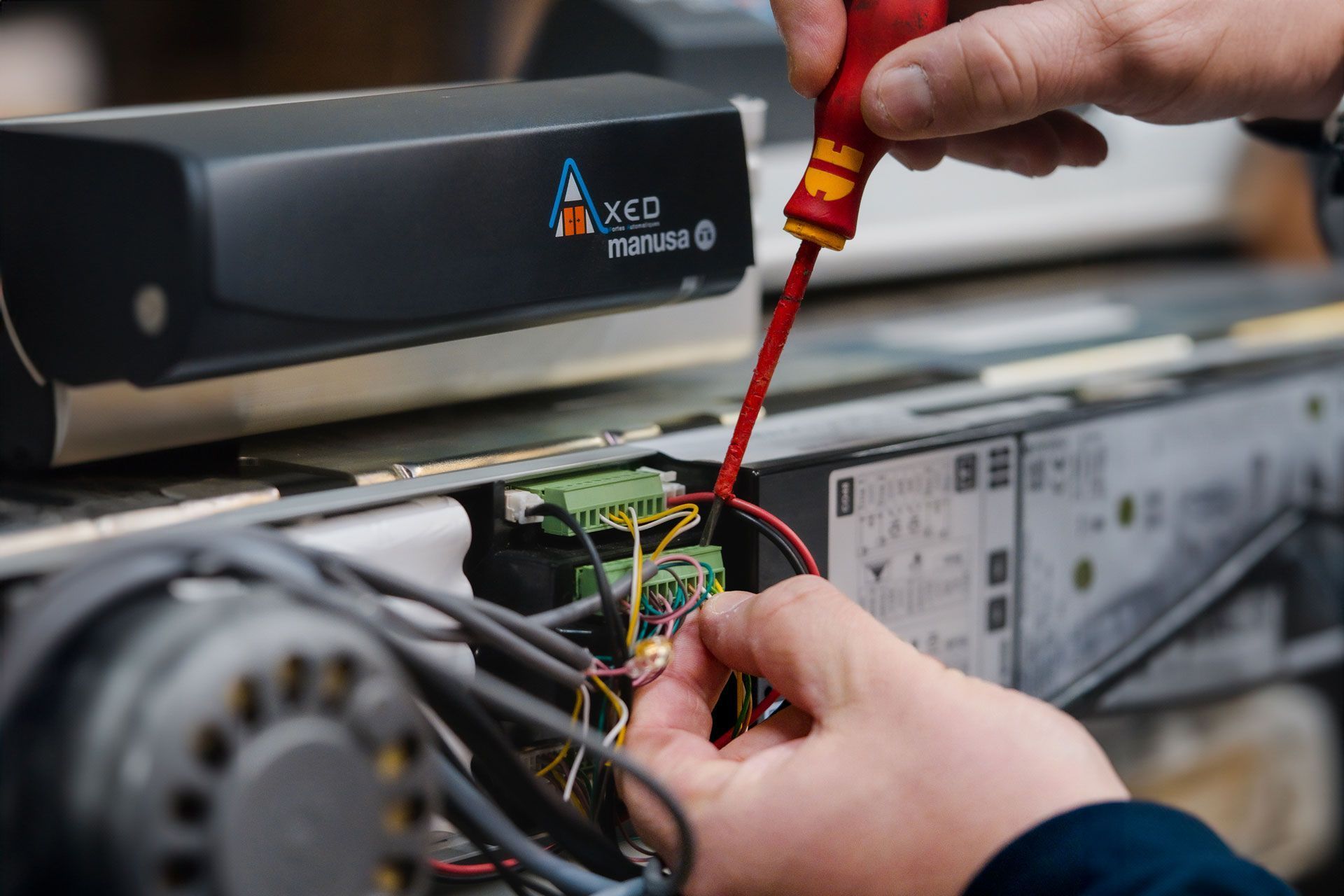 Des mains utilisent un tournevis à manche rouge pour ajuster le câblage d'un panneau de commande technique comportant un composant de marque Xeo.