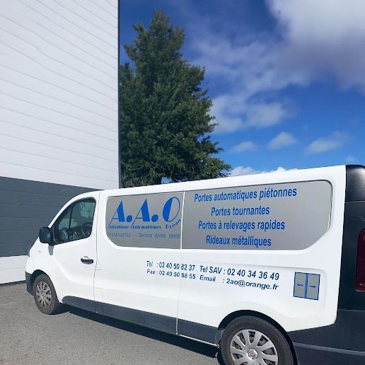 Camionnette de service blanche de la société AAO garée à côté d'un bâtiment, présentant des services spécialisés d'installation de portes et de portails métalliques.