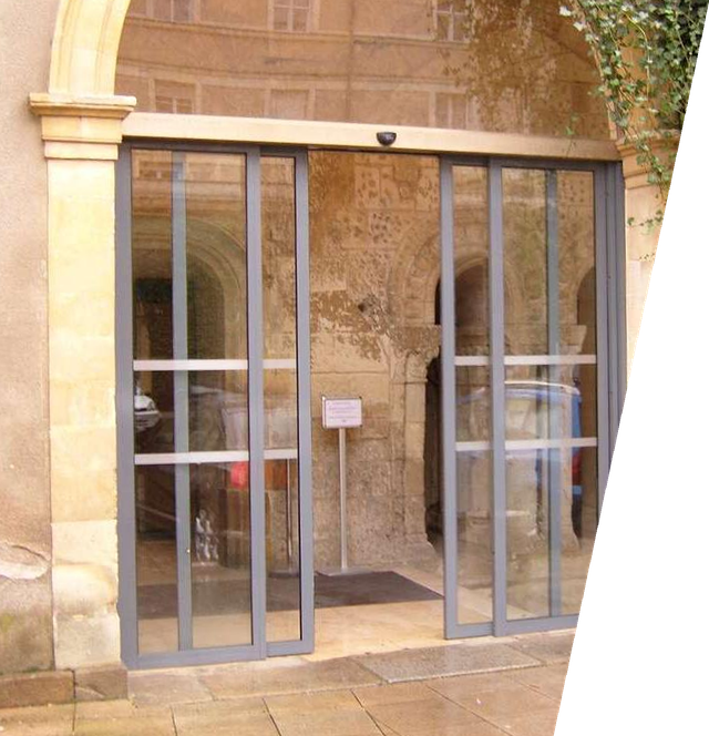 Une porte coulissante automatique en verre, encastrée dans une arche en pierre.
