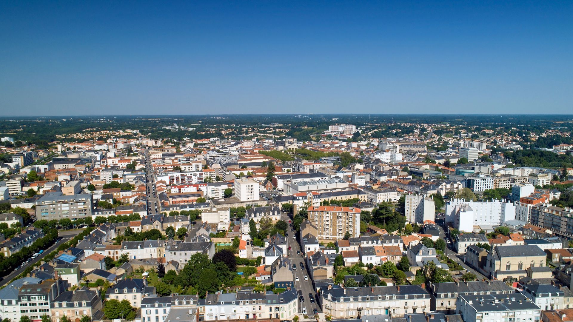 Vue aérienne en plongée d'une ville française dense, avec de nombreux bâtiments, sous un ciel bleu clair.
