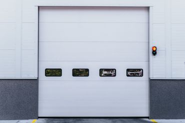 Une porte sectionnelle industrielle blanche fermée, avec quatre fenêtres rectangulaires et un feu de signalisation allumé sur la droite.