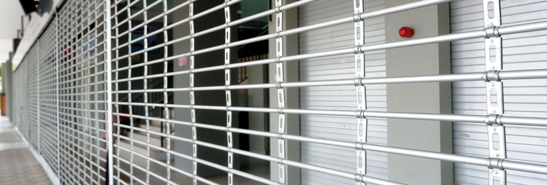Vue en perspective d'une longue grille de sécurité métallique à enroulement recouvrant la façade d'un magasin.
