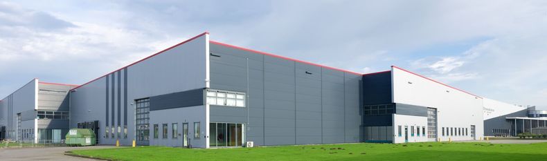 Un entrepôt industriel moderne de plain-pied, avec un revêtement gris, des portes d'entrée vitrées et une pelouse verte à l'avant.