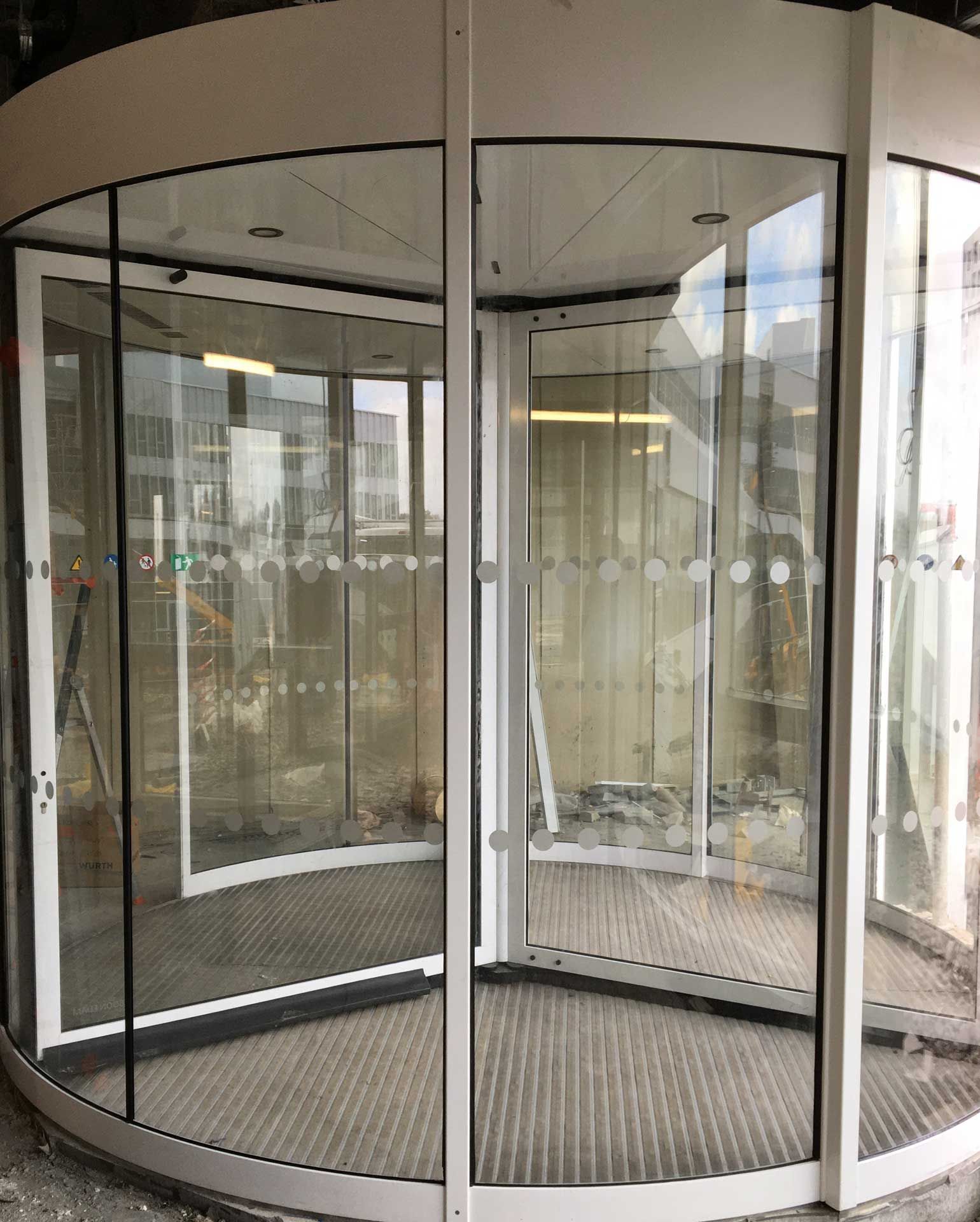 Une porte tournante en verre à cadre blanc avec des autocollants de sécurité circulaires sur les vitres.