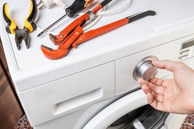 Un technicien, agenouillé sur un sol carrelé, utilise une perceuse électrique pour réparer un four mural.