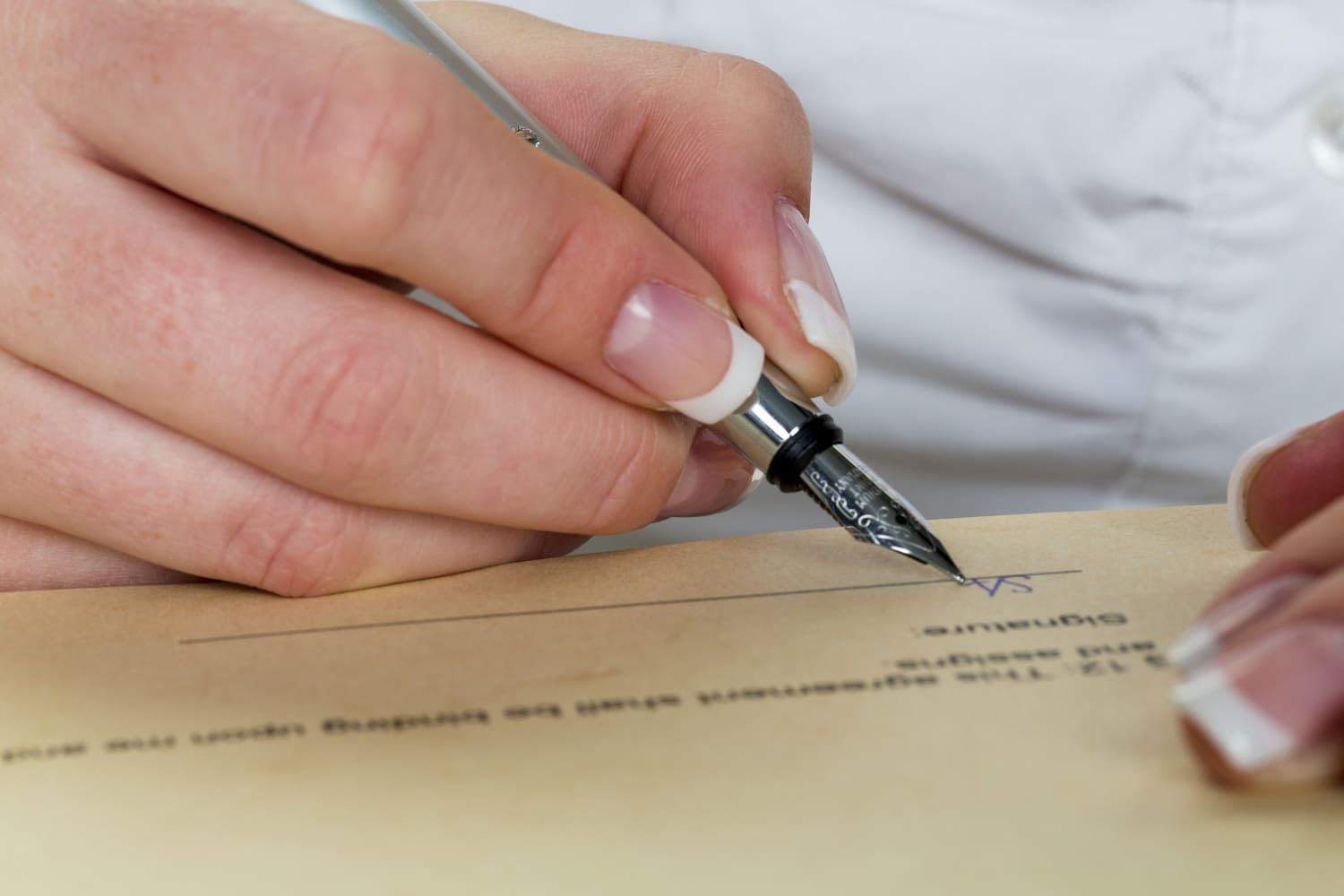 Una persona está escribiendo en un trozo de papel con una pluma estilográfica.