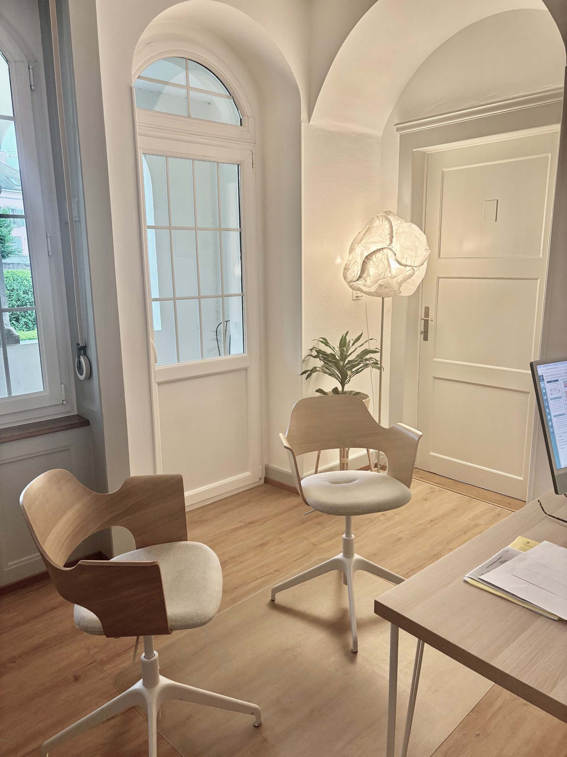Bureau lumineux à domicile avec deux chaises, un bureau, un lampadaire, une fenêtre cintrée et une plante en pot.