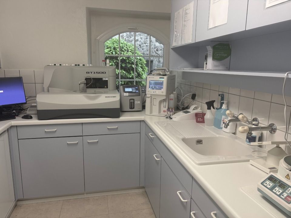 Comptoir de laboratoire de clinique avec équipement médical, évier, armoires et vue sur la verdure par la fenêtre.