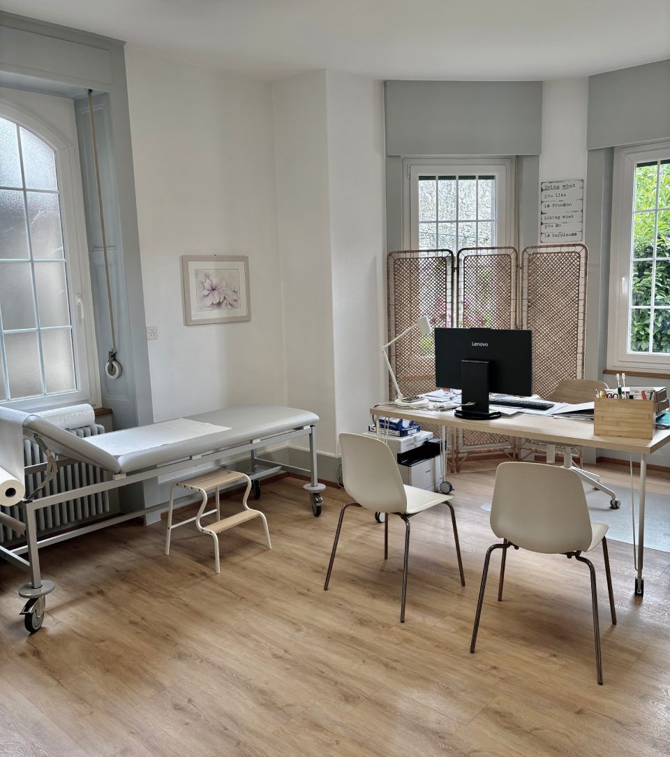 Bureau à domicile lumineux avec bureaux, chaises, écran d'ordinateur et table de massage près de grandes fenêtres.