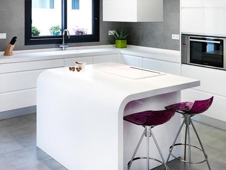 Cocina moderna blanca con isla, ventana negra, horno empotrado y dos taburetes morados.
