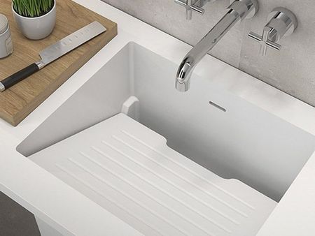 Fregadero de cocina blanco con grifo cromado y una tabla de secado acanalada integrada en la cubeta.