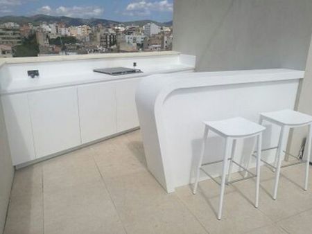 Balcón moderno de color blanco con mostrador incorporado, dos taburetes y vistas a la ciudad a través de la barandilla de cristal.