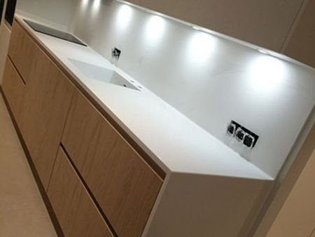 Encimera de cocina moderna con fregadero, salpicadero blanco, luces bajo los armarios y armarios de madera.