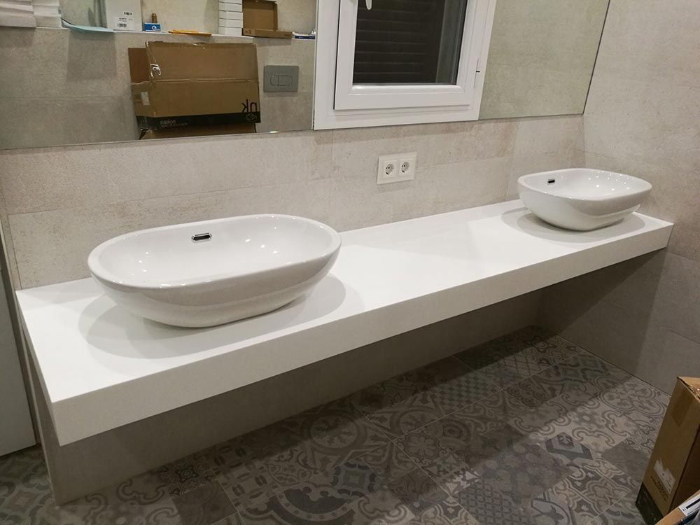 Tocador de baño moderno con dos lavabos blancos sobre encimera y una larga encimera blanca.