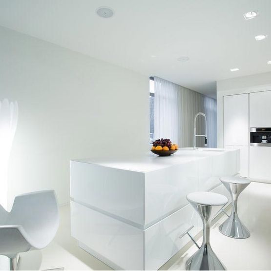 Cocina moderna de color blanco brillante con isla, taburetes y frutero sobre la encimera.