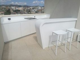 Barra de bar exterior moderna de color blanco con dos taburetes y una vista panorámica de la ciudad al fondo.