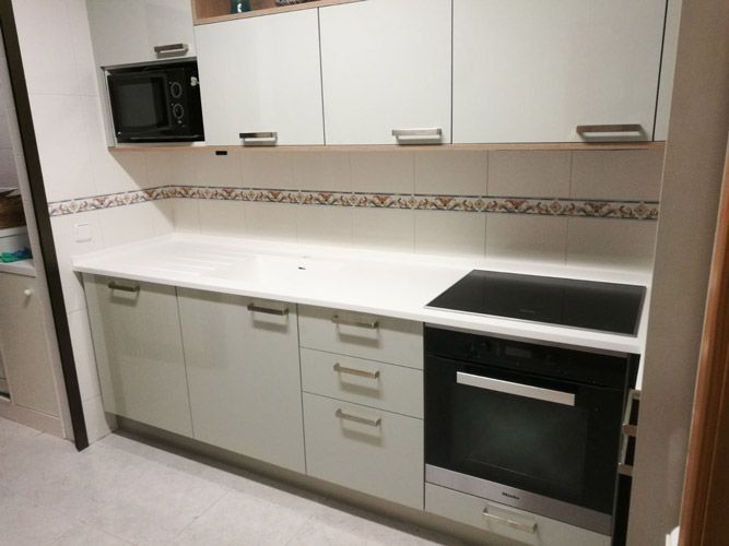 Cocina moderna blanca con microondas, vitrocerámica, horno y armarios empotrados.