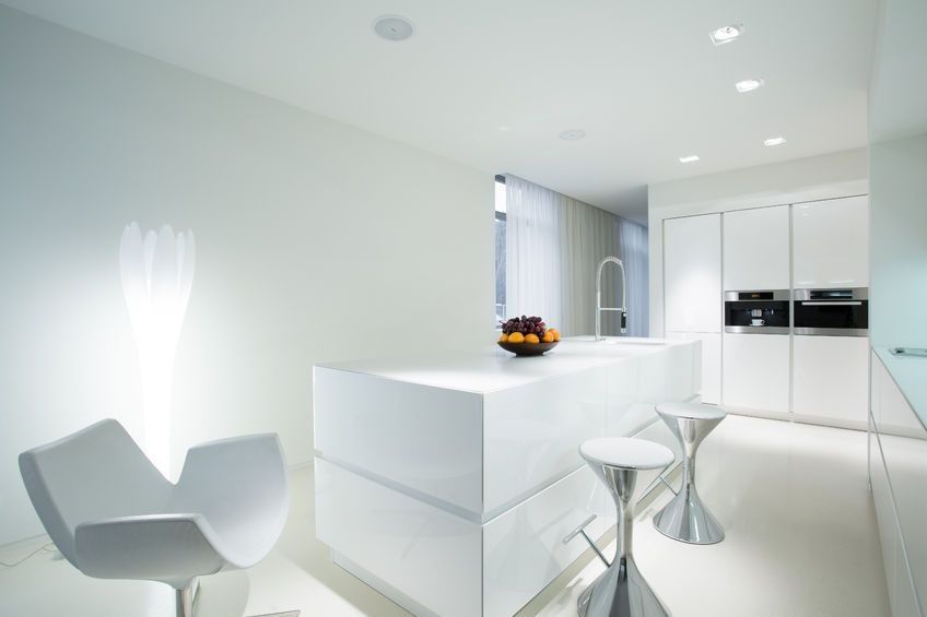 Cocina moderna minimalista blanca con isla curva, sillas transparentes y electrodomésticos integrados.