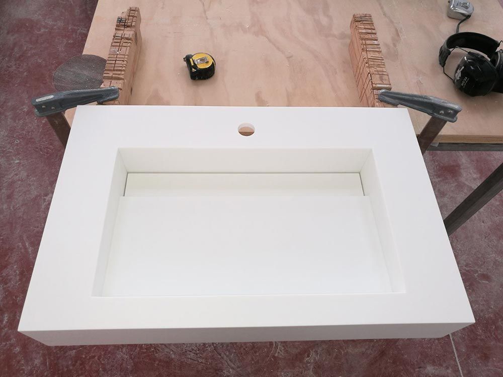 Fregadero o frontal de mueble rectangular blanco sobre un banco de trabajo con cinta métrica y abrazaderas al fondo.