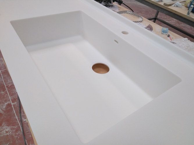 Lavabo rectangular blanco instalado sobre una encimera con desagüe central.