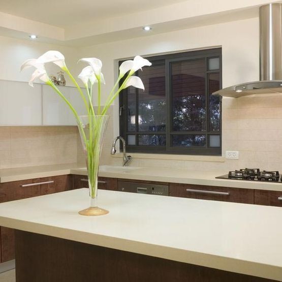 Cocina moderna con isla blanca, gabinetes oscuros, estufa de gas y jarrón con flores blancas.