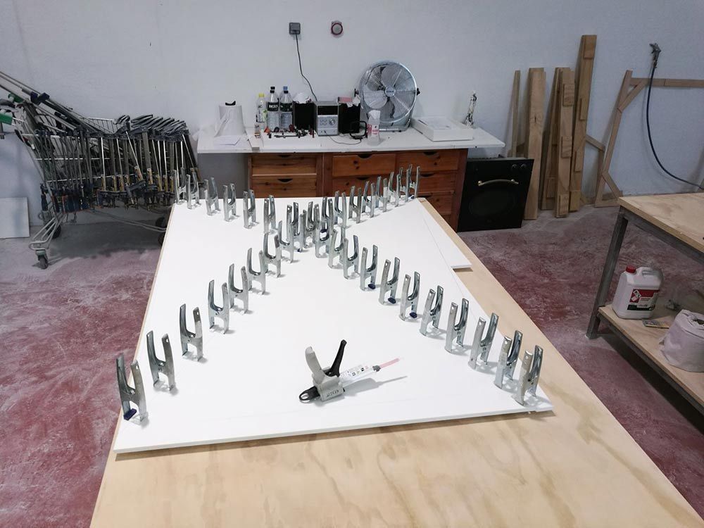 Mesa de taller con filas de tornillos metálicos sobre una pizarra blanca, en un taller desordenado.