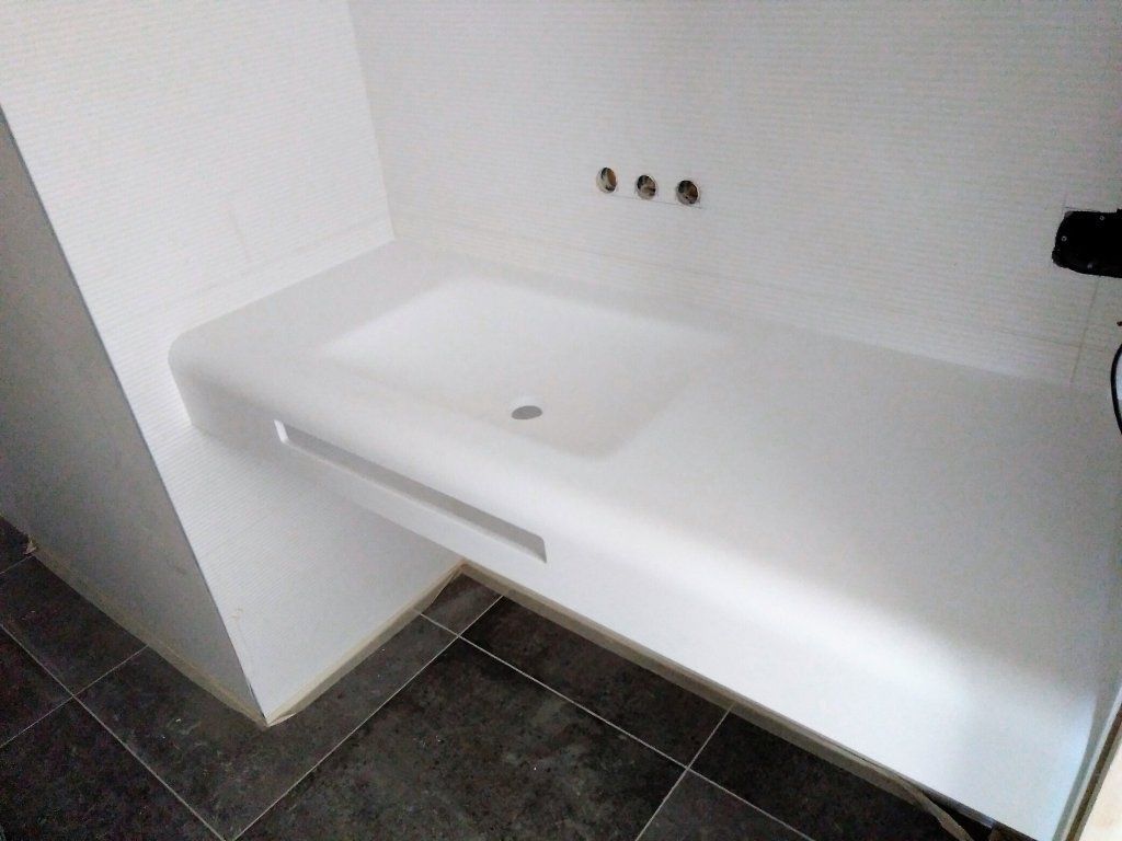 Lavabo minimalista blanco montado en la pared en un baño alicatado con baldosas oscuras en el suelo y grifería en la parte superior.