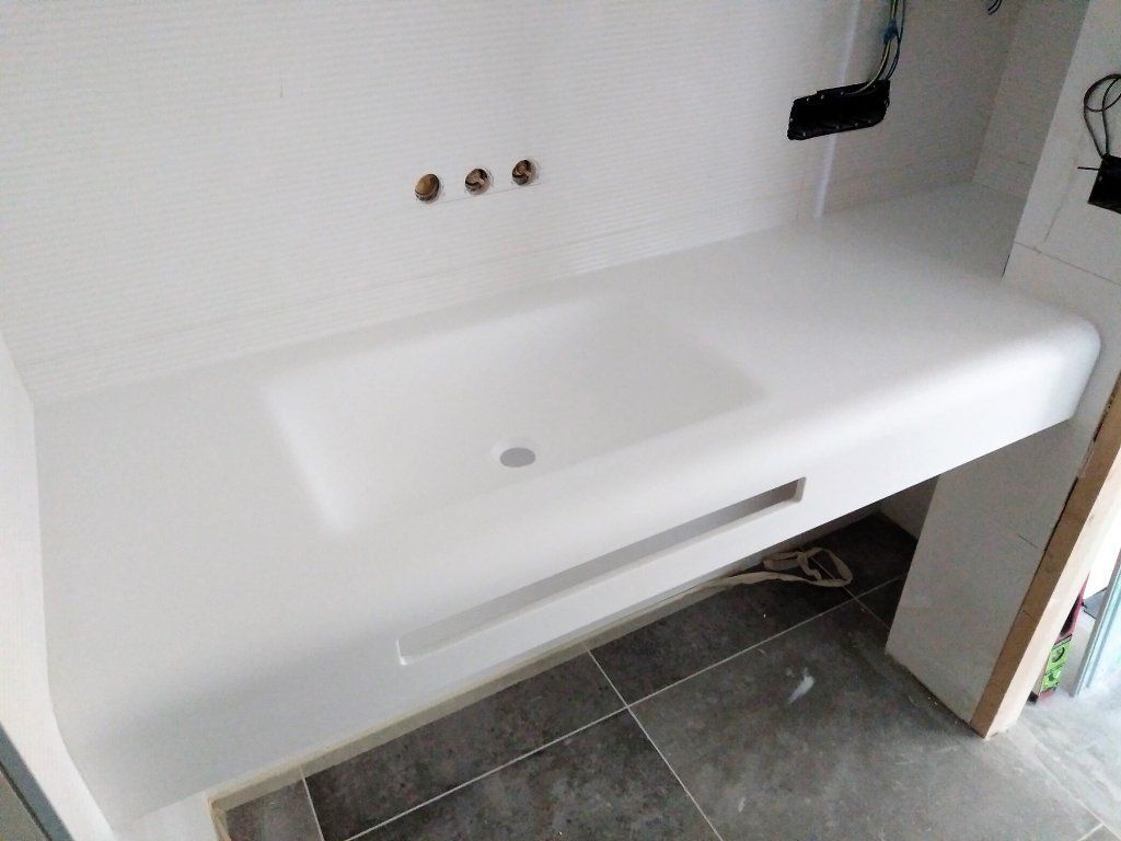 Lavabo blanco de pared con un solo grifo en un baño alicatado.