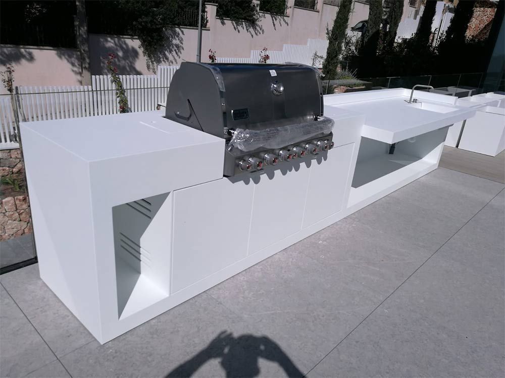 Encimera blanca de exterior con parrilla de acero inoxidable integrada en un patio.
