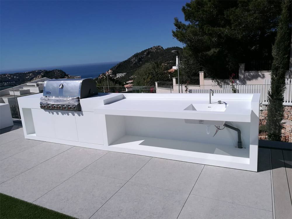 Patio exterior moderno con parrilla y fregadero blancos integrados, con vistas al océano y a las colinas.