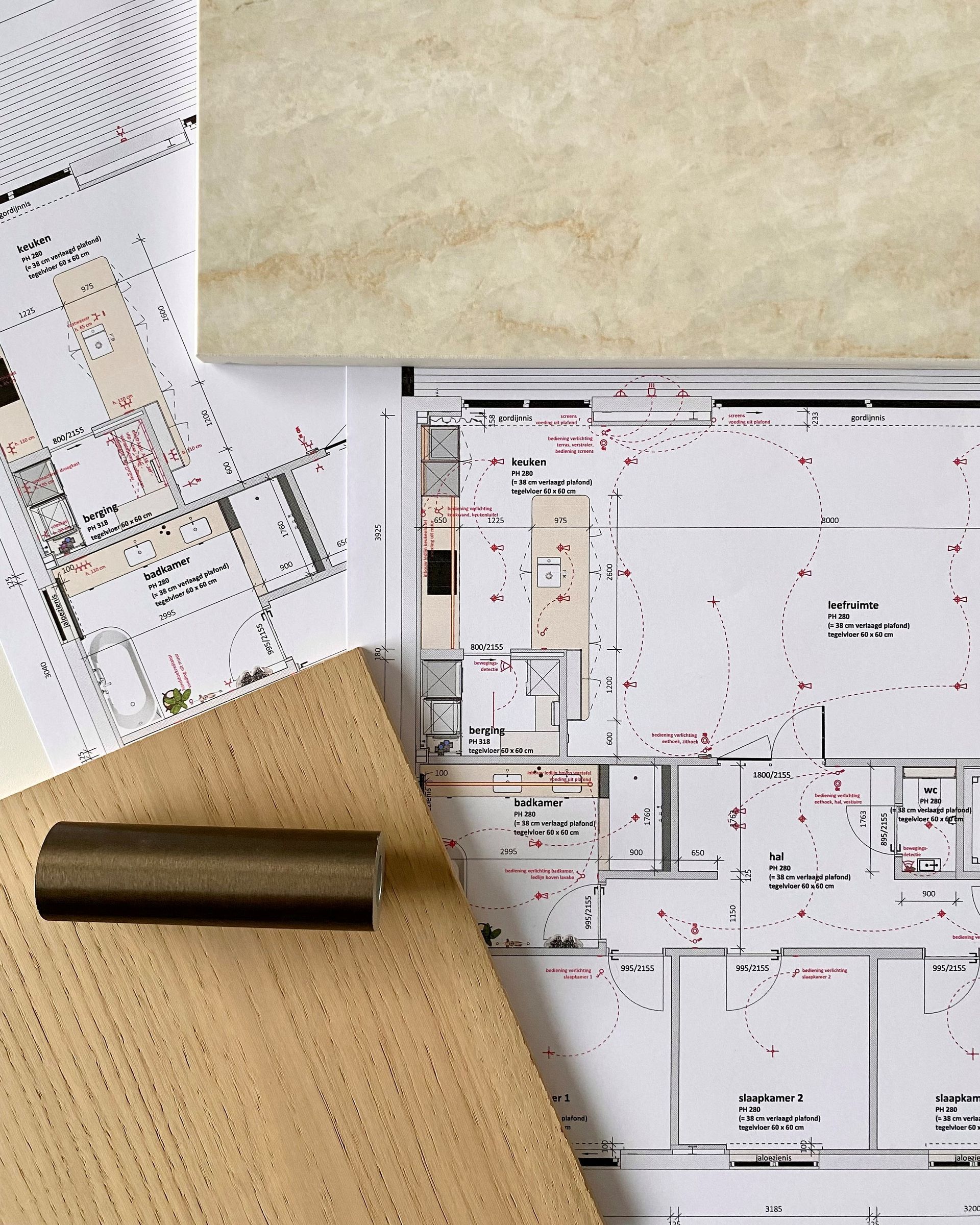 Architectonische plattegronden en stofstalen op een bureau met een houtmonster en een houder voor een zwarte pennen.