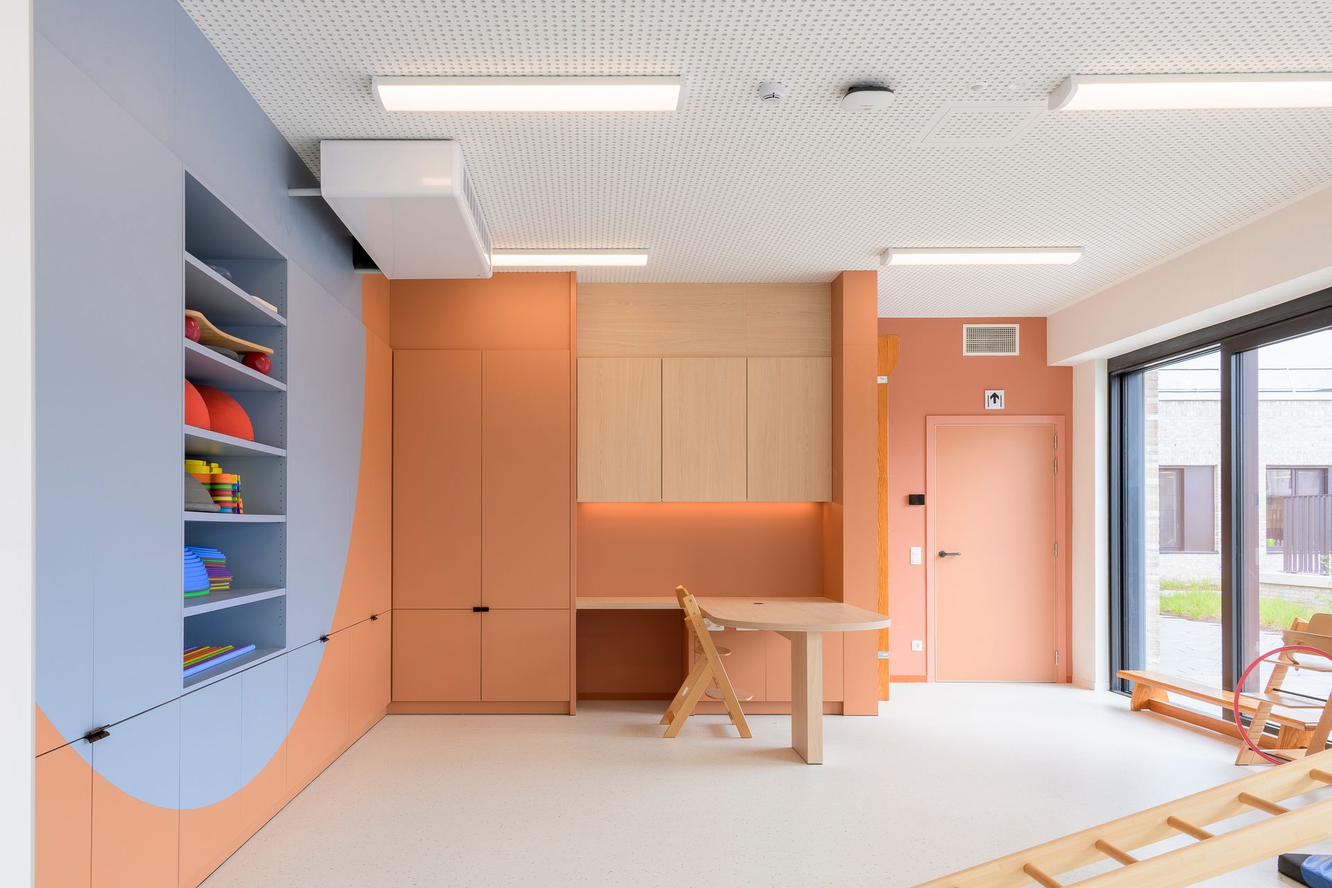 Moderne kamer met perzikkleurige kastjes, blauwe planken, een houten tafel en grote ramen.